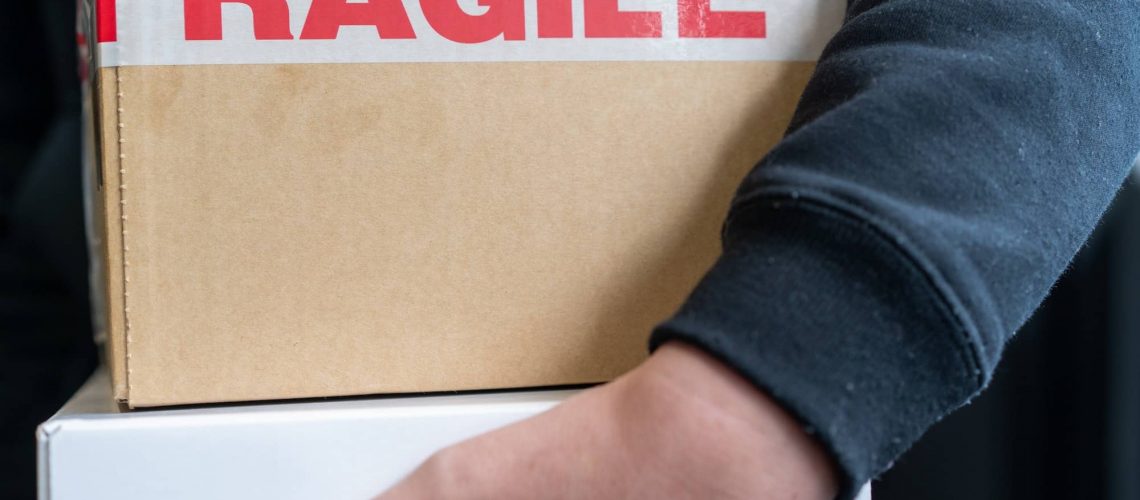 person holding a cardboard box with packaging tape saying fragile